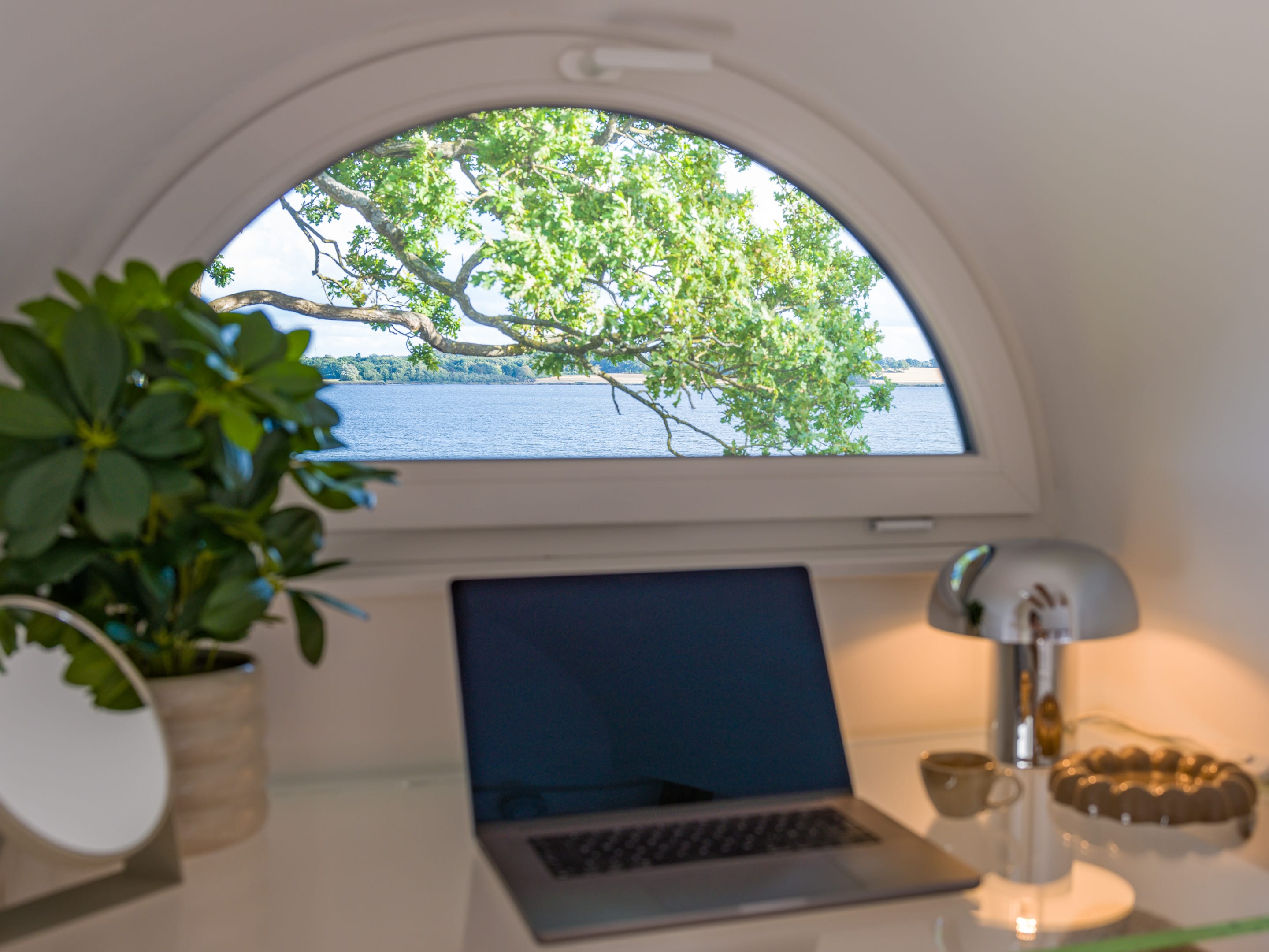 Glasschreibtisch unter dem Rundbogenfenster der Gaube mit Schleiblick